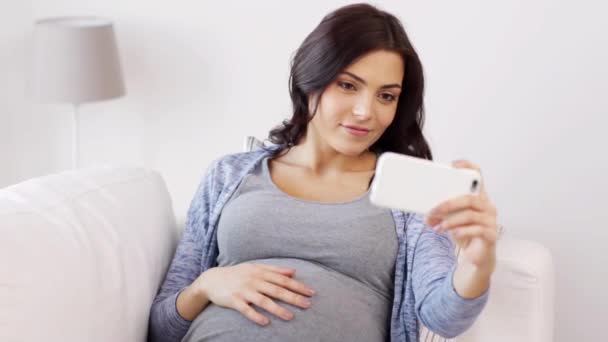 Беременная женщина делает селфи на смартфоне дома — стоковое видео