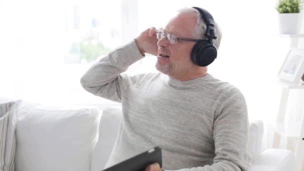 Starszy człowiek z komputera typu tablet i słuchawki w domu — Wideo stockowe