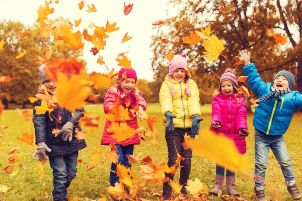 Счастливые дети играют с осенними листьями в парке — стоковое фото
