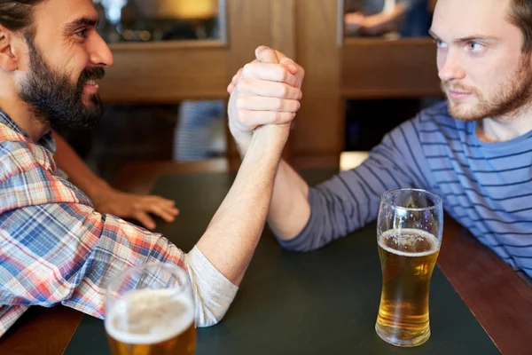 Gelukkige mannelijke vrienden arm worstelen in bar of pub — Stockfoto