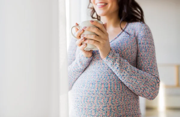 Närbild på gravid kvinna med te kopp på fönster — Stockfoto