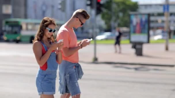 Feliz pareja adolescente con teléfonos inteligentes en la ciudad — Vídeo de stock