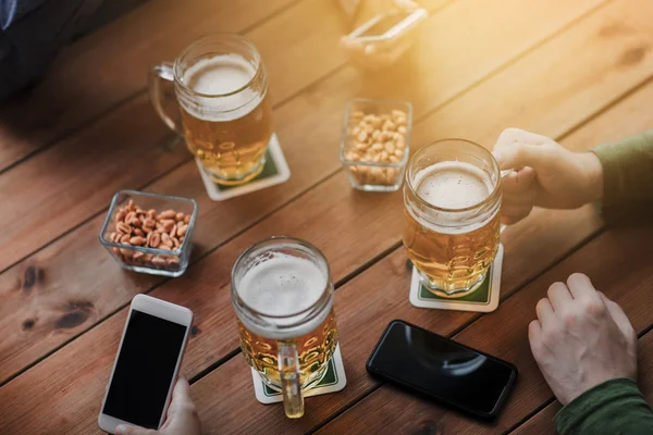 Close up of hands with smartphones and beer at bar — Stock Photo, Image