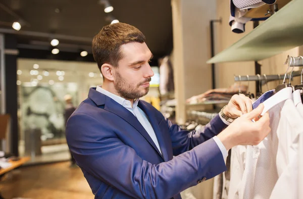 Gelukkig jonge man kiezen kleren in kledingwinkel — Stockfoto