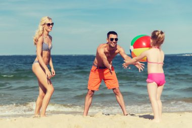 happy family playing with inflatable ball on beach clipart
