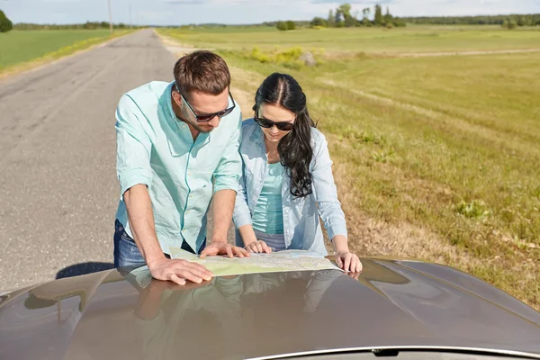 Homem feliz e mulher com mapa da estrada no capô do carro — Fotografia de Stock