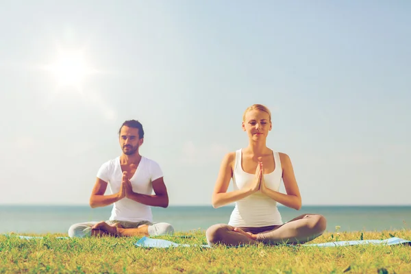 Sorrindo casal fazendo exercícios de ioga ao ar livre — Fotografia de Stock