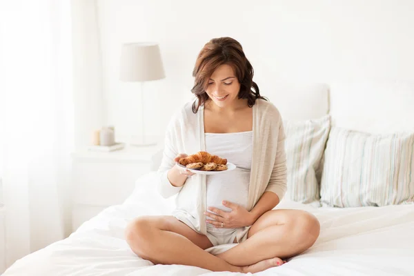 Glad gravid kvinna med croissant bullar hemma — Stockfoto