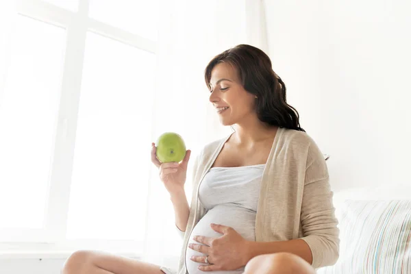 Happy pregnant woman eating green apple at home — Stock Photo, Image