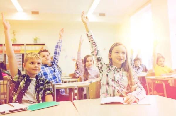 Grupo de escolares levantando las manos en el aula —  Fotos de Stock