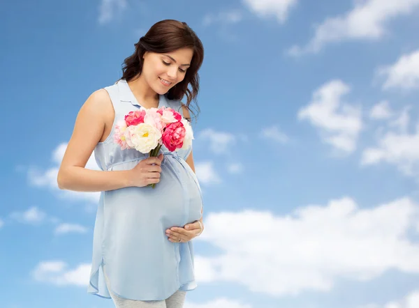 Mujer embarazada feliz con flores tocando el vientre —  Fotos de Stock