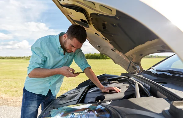 Homem com smartphone e carro quebrado no campo — Fotografia de Stock