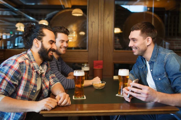 Друзья со смартфоном пьют пиво в баре — стоковое фото