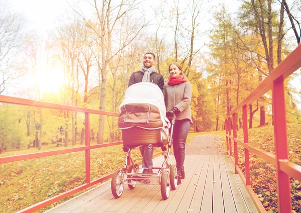 Smiling couple with baby pram in autumn park — Stock Photo, Image