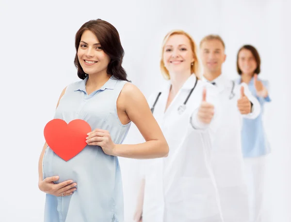 Счастливая беременная женщина с красным сердцем касаясь живота — стоковое фото