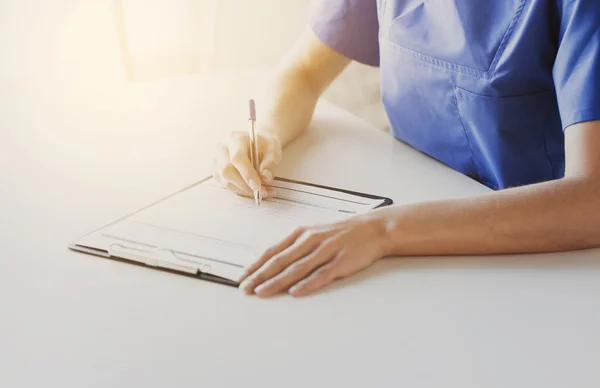 Close up of doctor or nurse writing to clipboard — Stock Photo, Image