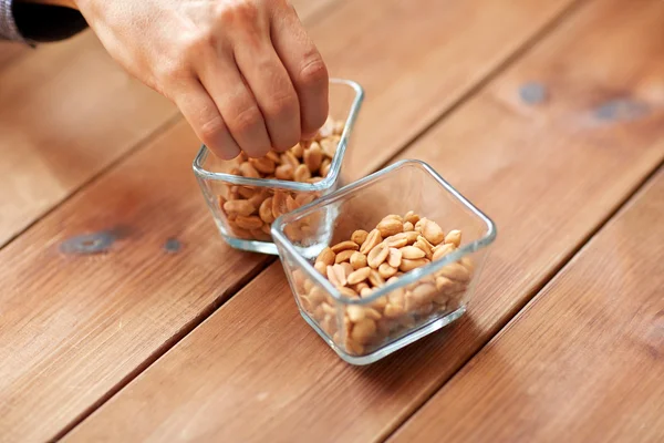 Närbild av hand tar jordnötter från skål på bordet Stockbild