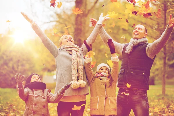 Lycklig familj spelar med hösten lämnar i park — Stockfoto