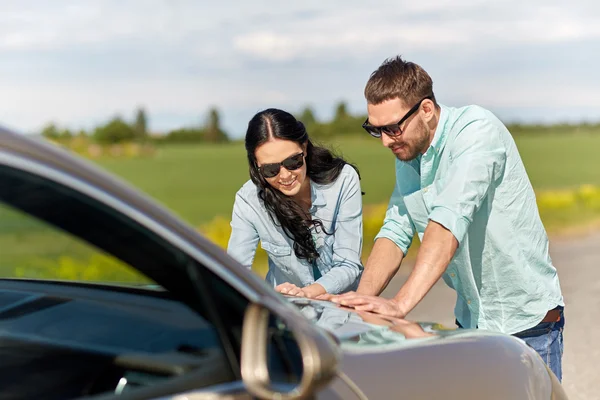 Счастливые мужчина и женщина с дорожной картой на капоте автомобиля — стоковое фото