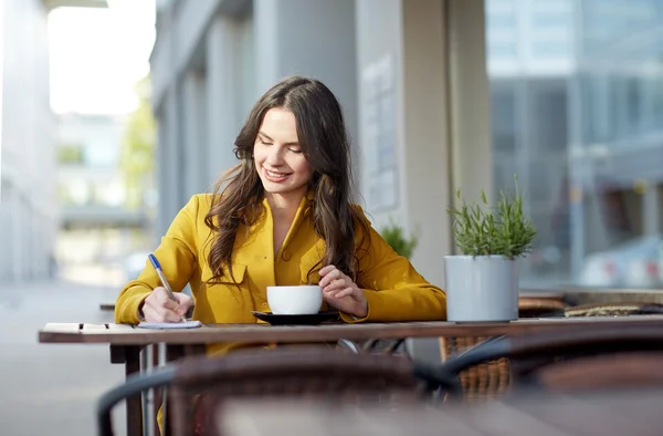 Glad kvinna med anteckningsboken dricka kakao på café — Stockfoto