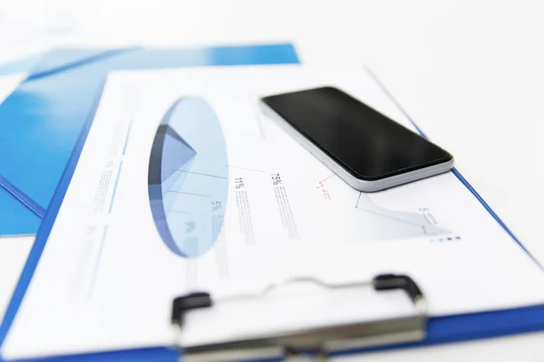 Close up of smartphone and clipboard with charts — Stock Photo, Image