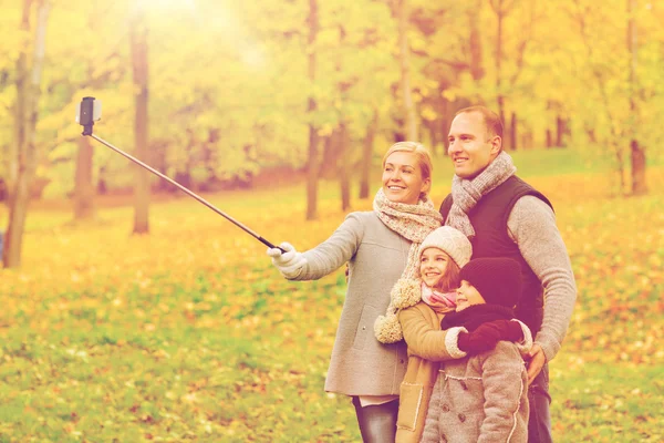 Happy family with smartphone and monopod in park — Stock Photo, Image