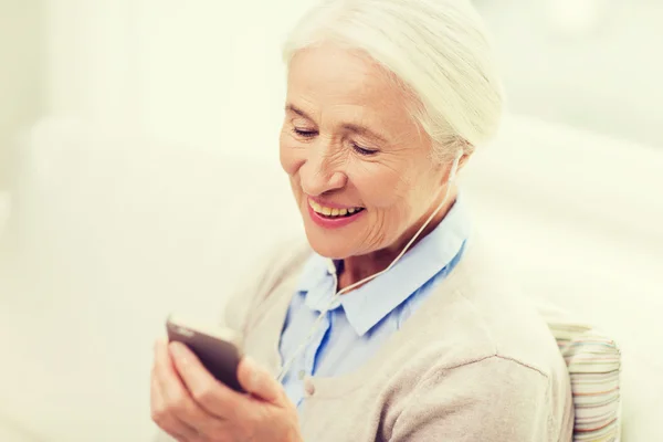 Senior woman with smartphone and earphones at home — Stock Photo, Image