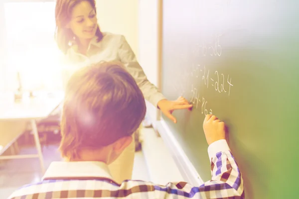 School boy with teacher writing on chalk board — Stockfoto