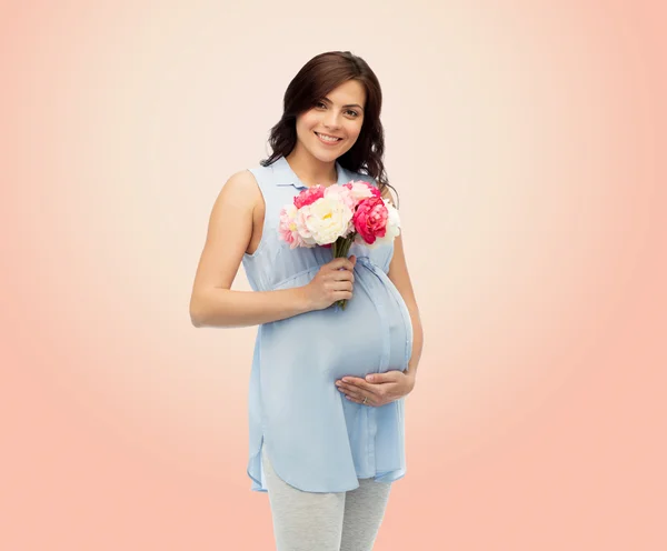 Heureuse femme enceinte avec des fleurs touchant le ventre — Photo