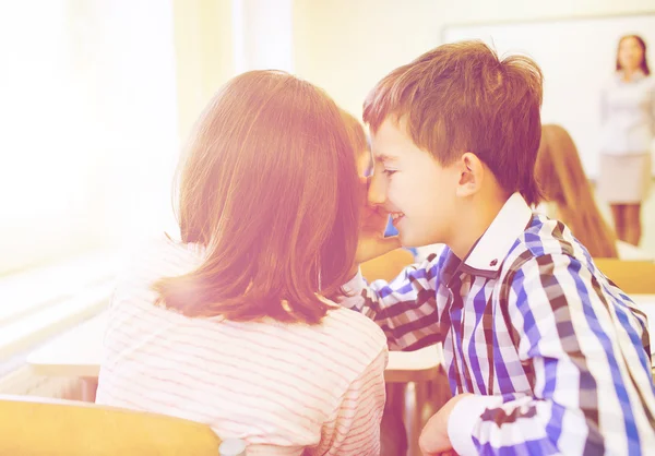 Glimlachend schoolmeisje aan klasgenoot oor fluisteren — Stockfoto