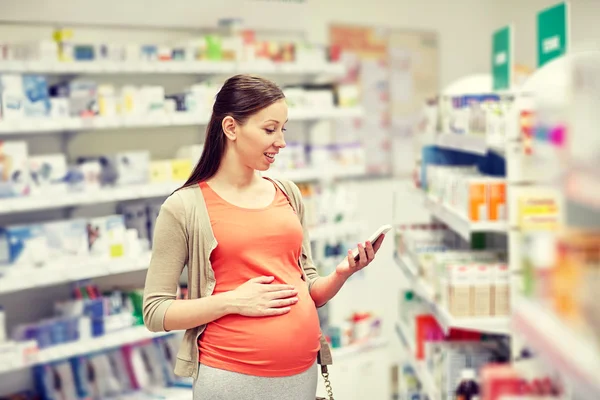 Mujer embarazada feliz con teléfono inteligente en la farmacia — Foto de Stock