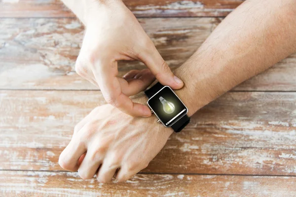 Close up of hands with light bulb on smart watch — Stock Photo, Image