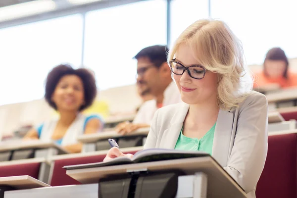 Student girl writing to notebook in lecture hall — Stock Photo, Image