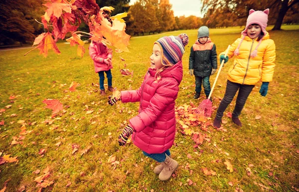 Счастливые дети играют с осенними листьями в парке — стоковое фото