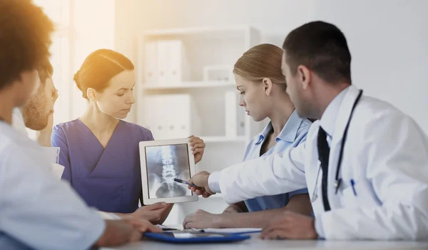 Arztgruppe mit Röntgenbild auf Tablet-PC in Klinik — Stockfoto