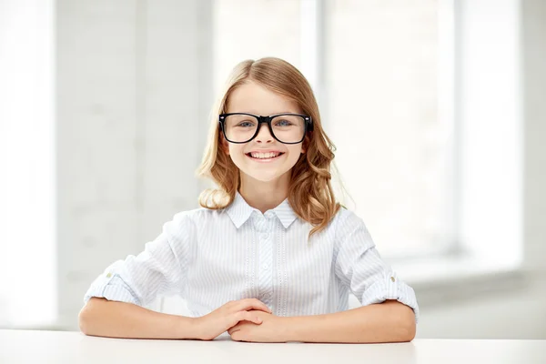 Gelukkig schoolmeisje in glazen zittend aan tafel — Stockfoto