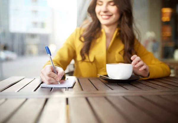 Ευτυχισμένη γυναίκα με το σημειωματάριο και cappucino στο café — Φωτογραφία Αρχείου