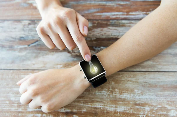 Close up of hands with light bulb on smart watch — Stock Photo, Image