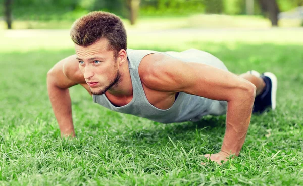 Mladý muž dělá push up na trávě v parku v létě — Stock fotografie