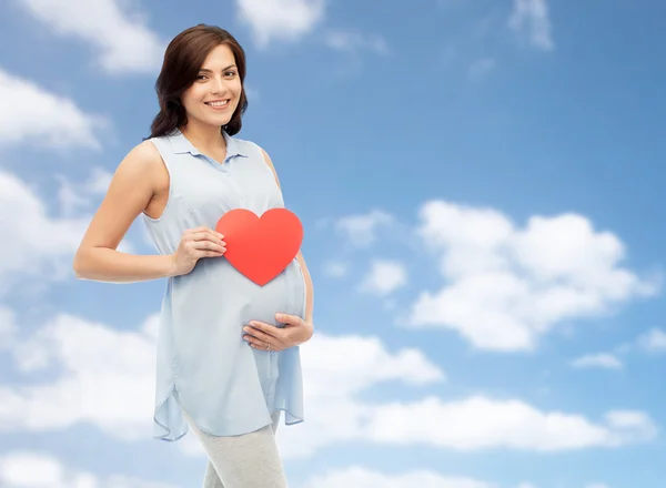 Mulher grávida feliz com coração vermelho tocando barriga — Fotografia de Stock