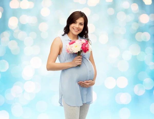 Mujer embarazada feliz con flores tocando el vientre — Foto de Stock