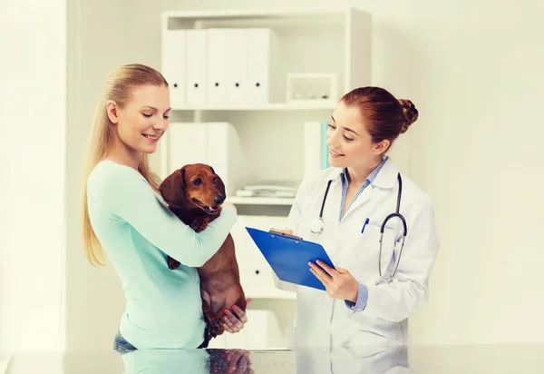 Happy woman with dog and doctor at vet clinic — Stock Photo, Image