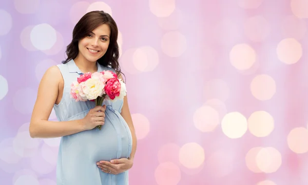 Счастливая беременная женщина с цветами касаясь живота — стоковое фото