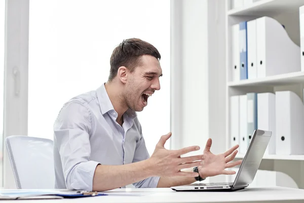 Сердитый бизнесмен с ноутбуком и бумагами в офисе — стоковое фото