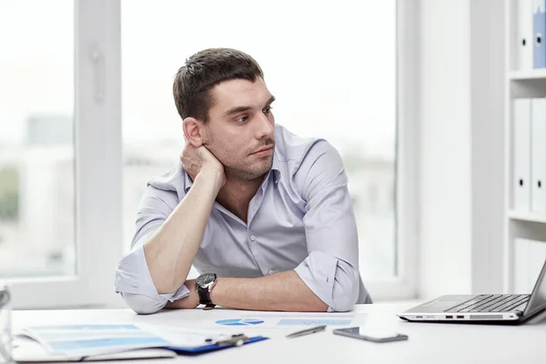 Uomo d'affari annoiato con computer portatile e carte in ufficio — Foto Stock