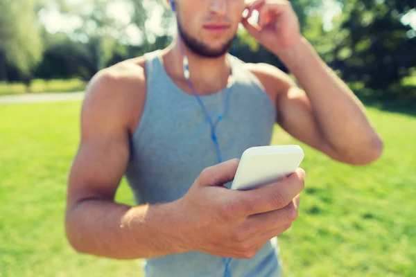 イヤホンと公園でスマート フォンを持つ若者 — ストック写真