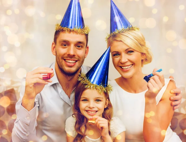 Usmívající se rodina v modré klobouky foukání laskavost rohy — Stock fotografie