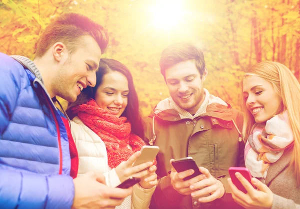 Smiling friends with smartphones in city park — Stock Photo, Image