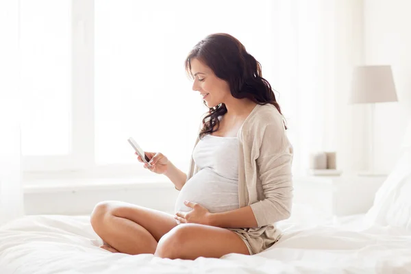 Mujer embarazada feliz con teléfono inteligente en la cama en casa — Foto de Stock