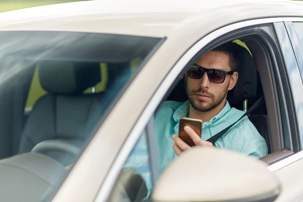 Homme en lunettes de soleil voiture de conduite avec smartphone — Photo